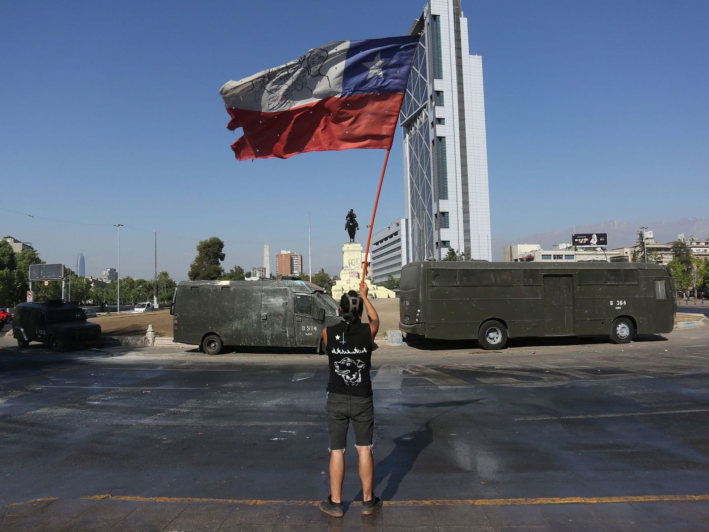Un hombre hondea una bandera mientras pasan camiones de carabineros durante una nueva protesta en contra del gobierno. (EFE)