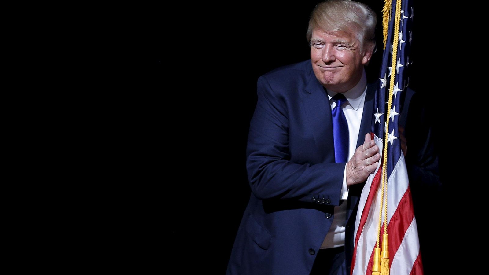 Foto: El candidato presidencial republicano Donald Trump abraza una bandera de EEUU durante un mitin electoral en Derry, New Hampshire, el 19 de agosto de 2015 (Reuters). 