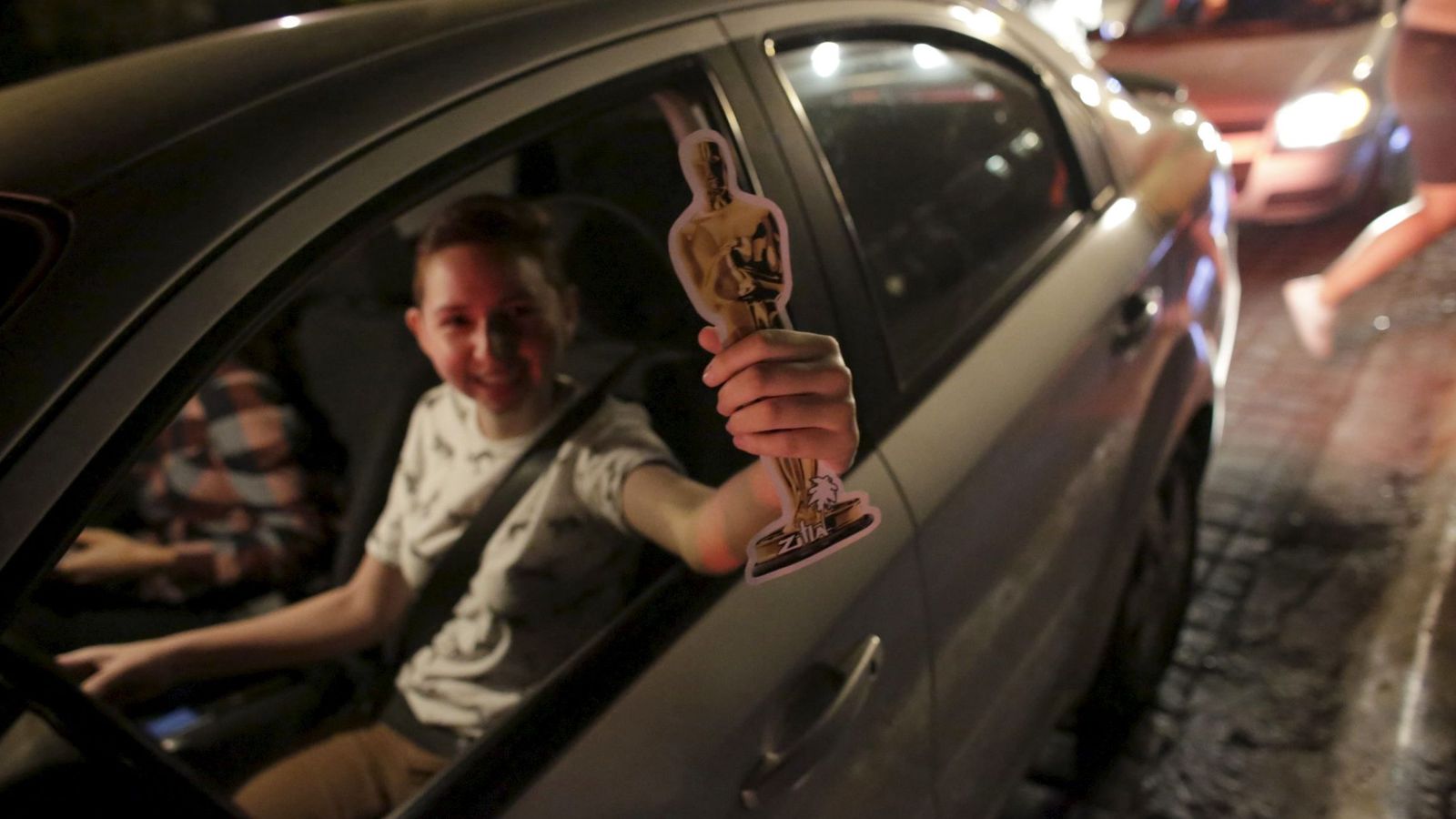 Foto: Un fan sostiene una réplica de un Oscar mientras pasea en coche (Reuters)