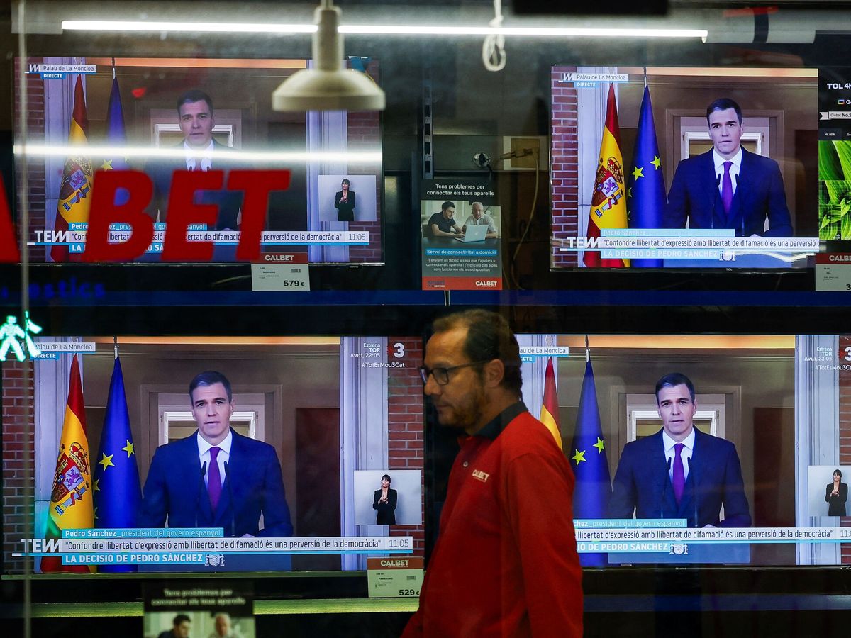 Foto: Una persona camina junto a unas televisiones que emiten la declaración del presidente del Gobierno, Pedro Sánchez. (Reuters/Albert Gea)