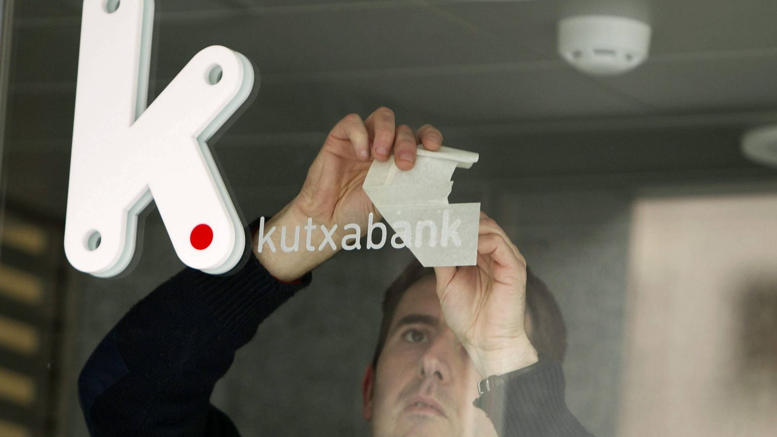 Foto: Un operario coloca en una oficina el rótulo con el logotipo de Kutxabank. (EFE)