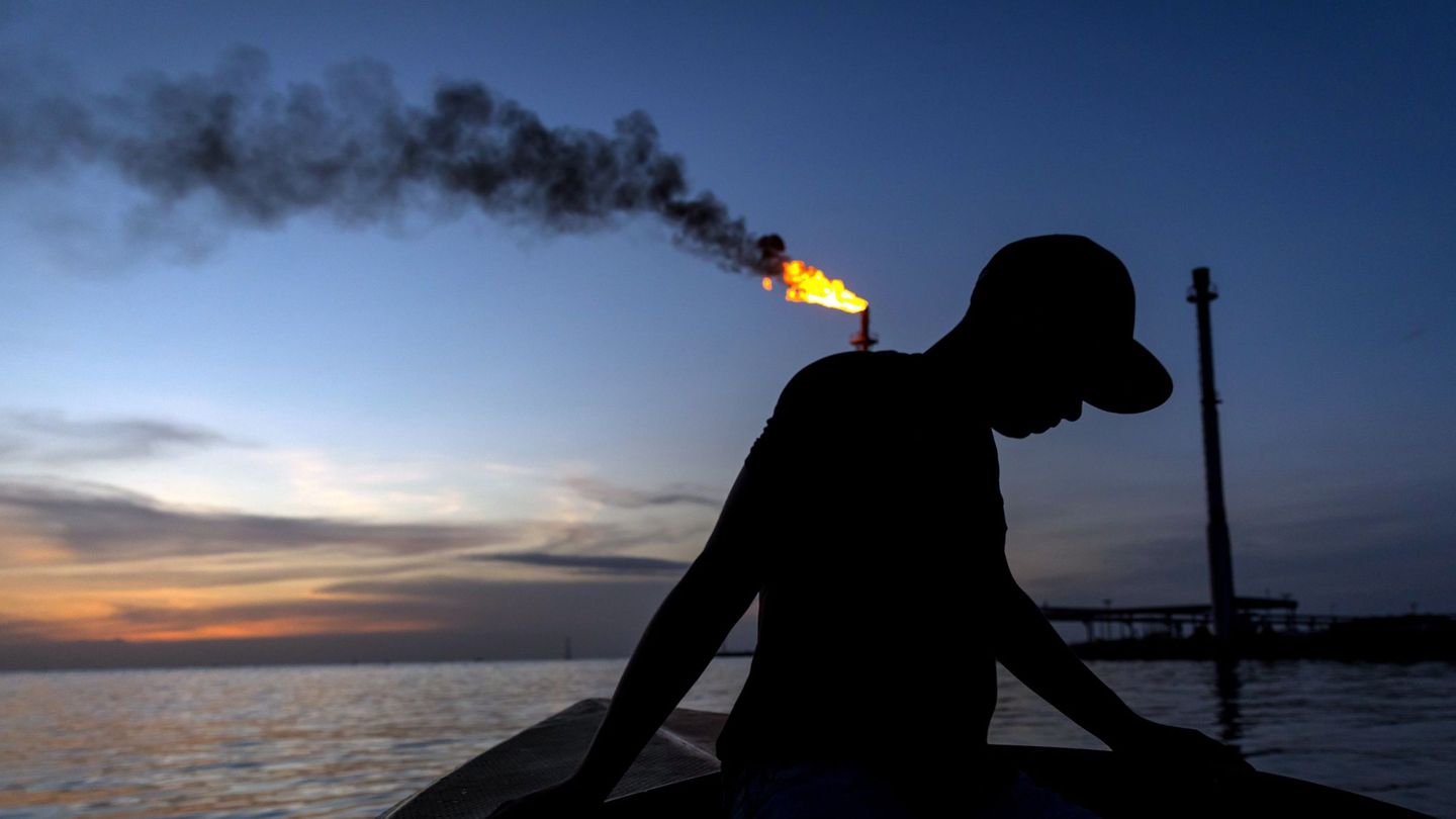 Un pescador en una lancha para la pesca nocturna de camarones, mientras pasa por un quemador de combustible llamado 'Mechurrio' en Venezuela. (EFE)