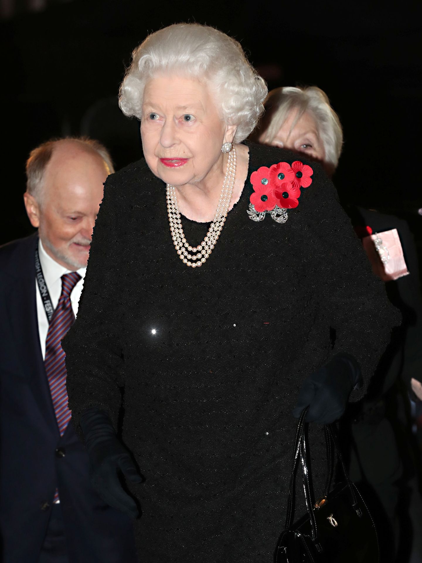 La reina Isabel II, también de negro, con collar de perlas y luciendo en la solapa, al igual que Kate y Meghan, flores de amapola. (Reuters)