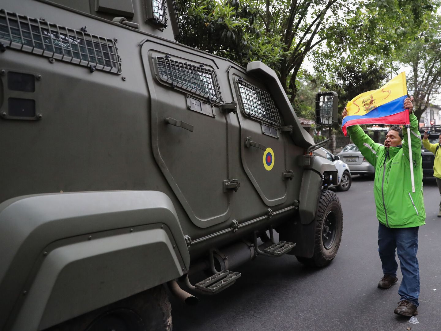Un hombre exhibe una bandera mientras pasa un vehículo blindado donde es trasladado el ex vicepresidente ecuatoriano Jorge Glas, este sábado en Quito (Ecuador). (EFE/José Jácome)