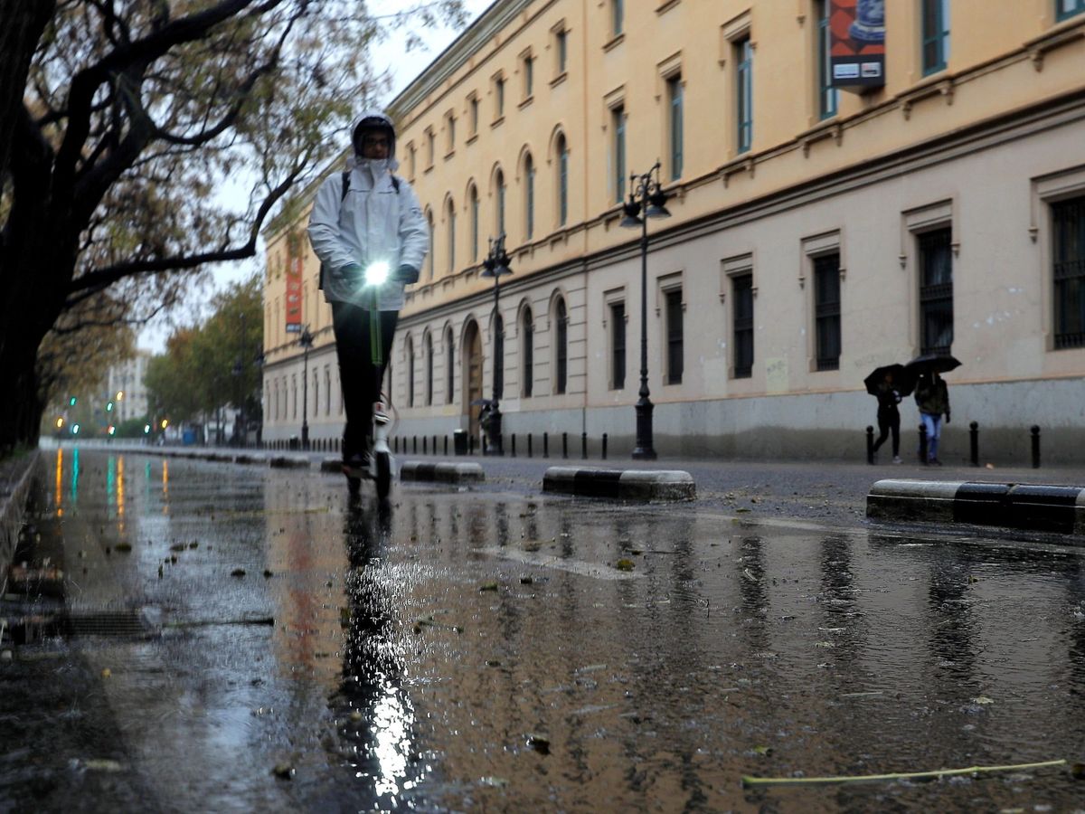 Foto: Una persona circula bajo la lluvia, en un patinete eléctrico, en Valencia. (EFE)