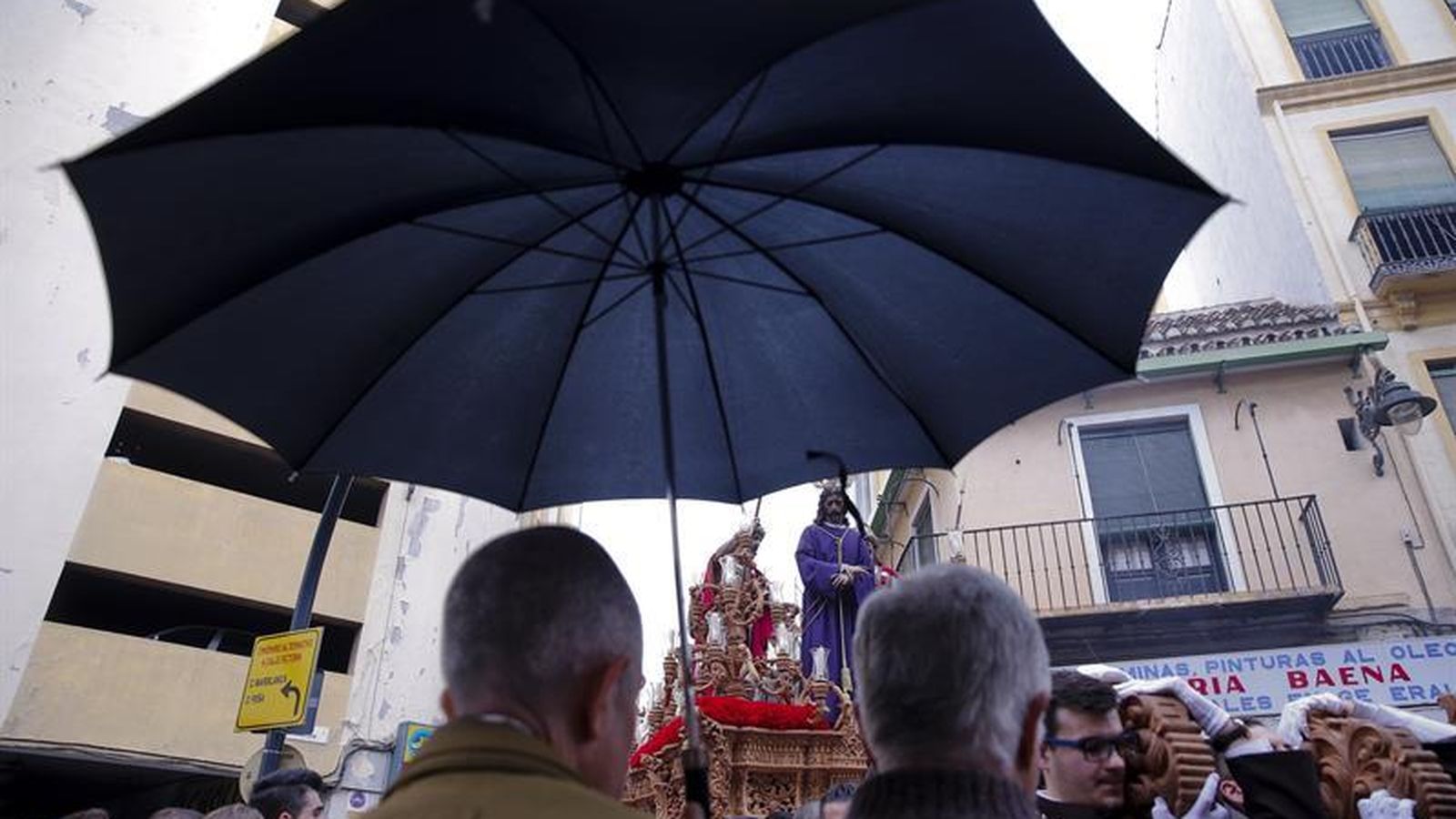 Foto: Varias personas se protegen de la lluvia bajo un paraguas ante el trono de la cofradía del Dulce Nombre, que se ha recogido del desfile procesional por la mala metereología la tarde del Domingo de Ramos en Málaga. EFE/ Jorge Zapata