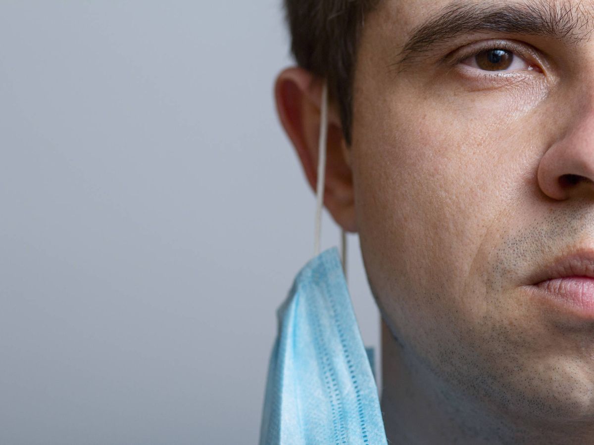 Foto: Media cara de un hombre con la mascarilla pendiendo de una oreja. (iStock)