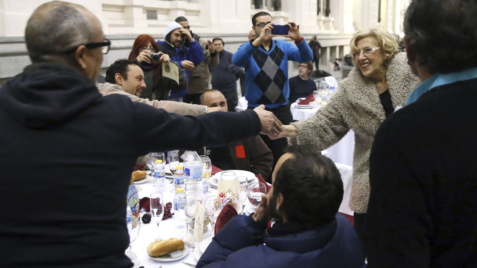 Foto: La alcaldesa de Madrid, Manuela Carmena (d), saluda a algunas de las 200 personas sin hogar que cenaron en el Palacio de Cibeles. (EFE)