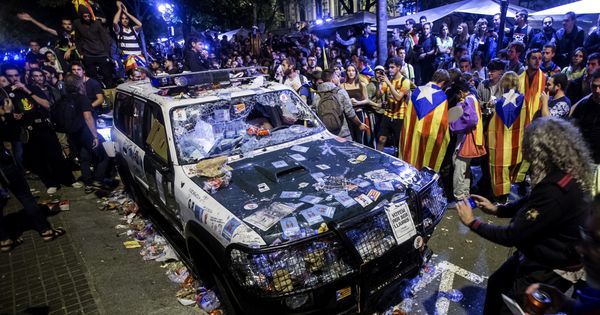 Foto: Numerosas personas rodean un coche de la Guardia Civil destrozado y repleto de pegatinas que realizaba un registro en la Conselleria de Economía con motivo del 1-O. (EFE)