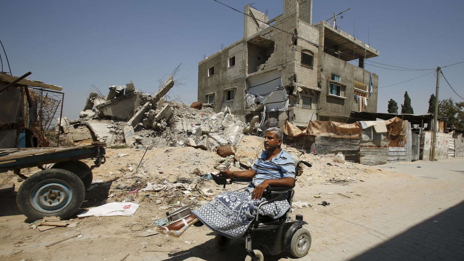 Foto: Un profesor palestino pasea en silla de ruedas frente a su casa en ruinas. (Reuters)