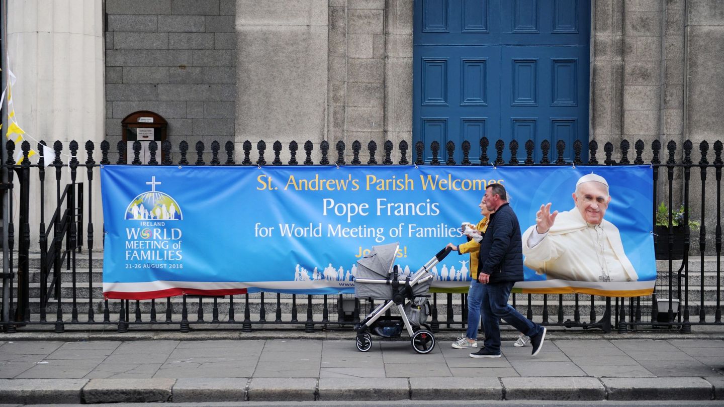 Una familia camina delante de una pancarta con la imagen del papa Francisco situada fuera de una iglesia en Dublín. (EFE)