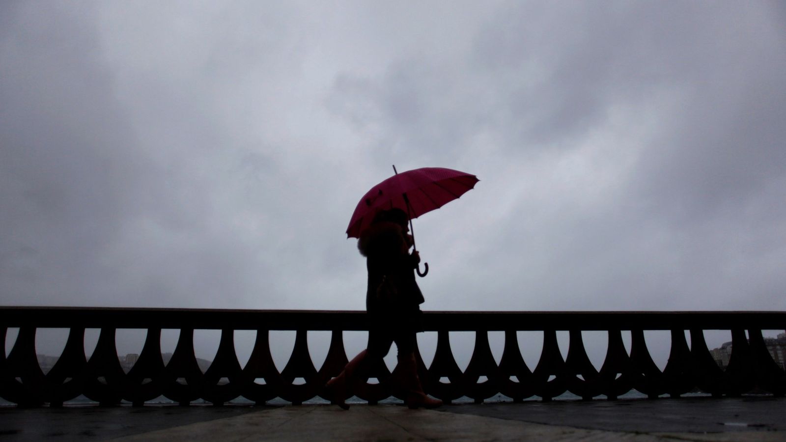 Foto: Una mujer camina bajo la lluvia por el paseo marítimo de A Coruña. (EFE)