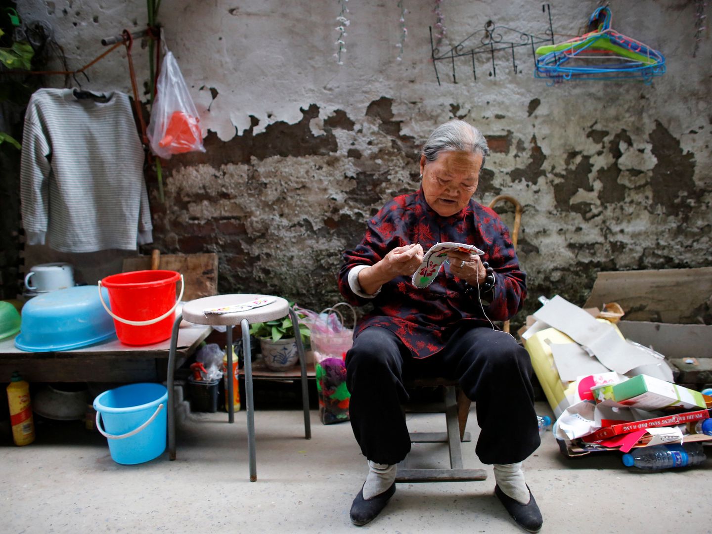 La señora Zhong, una inmigrante rural, remienda zapatos en el patio de su casa en el extrarradio de Pekín, el 1 de octubre de 2017. (Reuters)