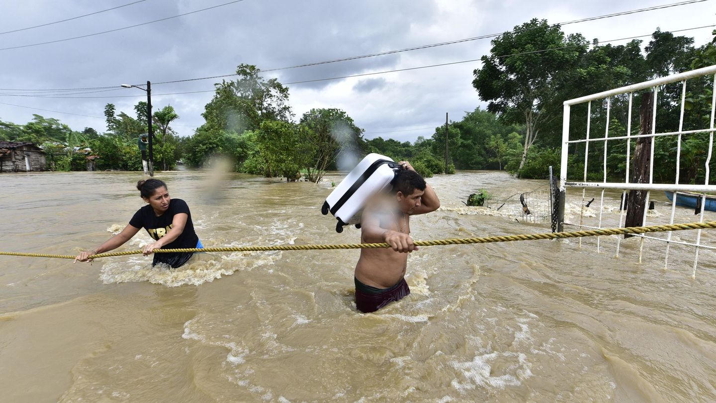 Dos personas tratan de cruzar una zona inundada por el desborde de los ríos hoy, en la sierra de Tabasco (México). (EFE)