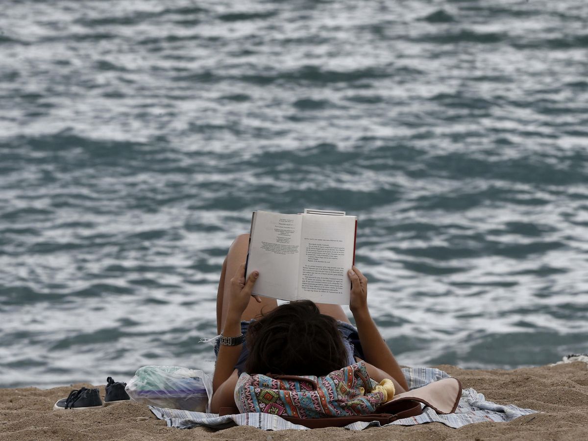 Foto: Una joven disfruta de la lectura de un libro en la playa de la Barceloneta. (EFE)