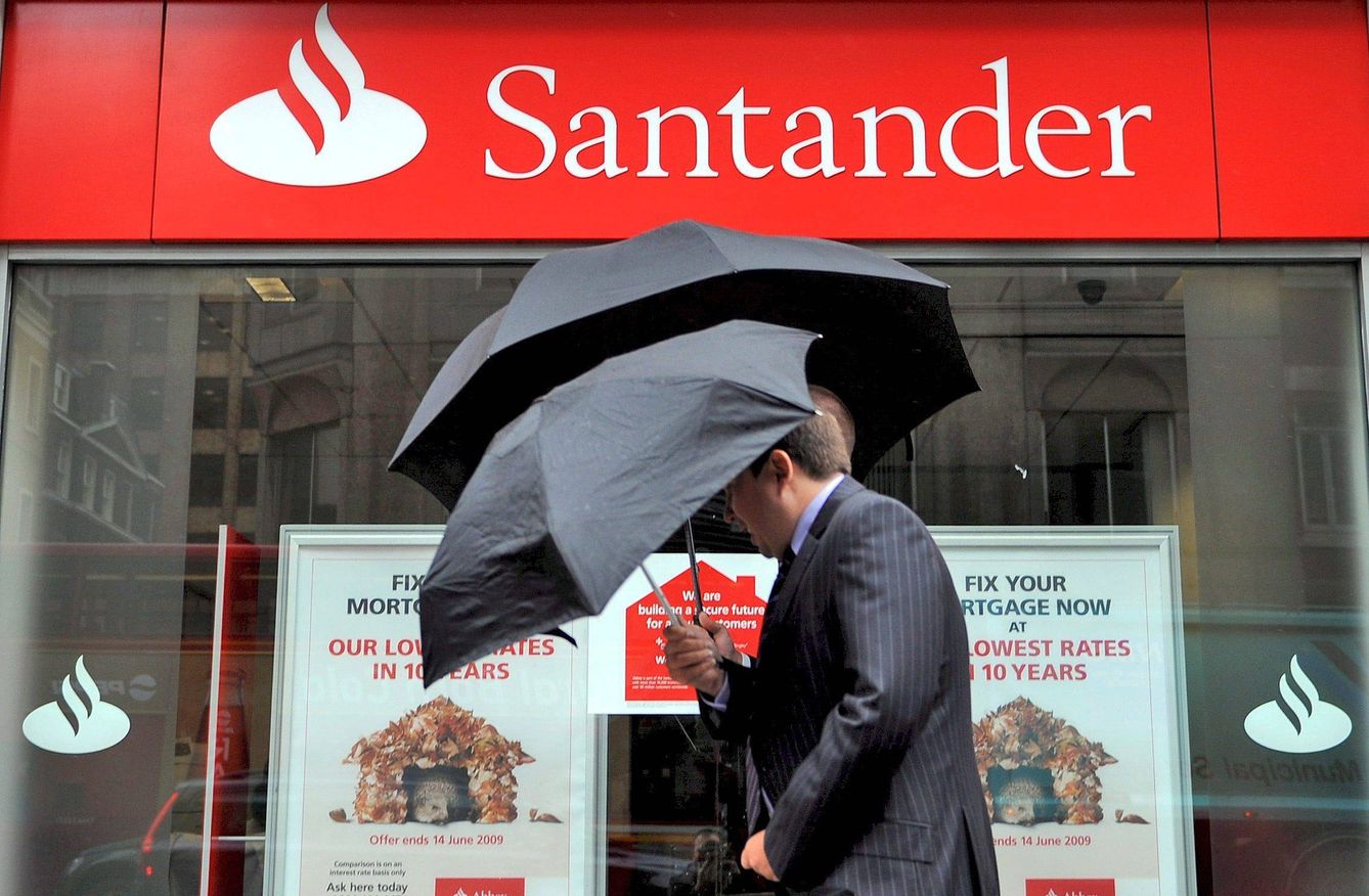 Dos hombres caminan junto a una oficina del Banco Santander. (EFE)