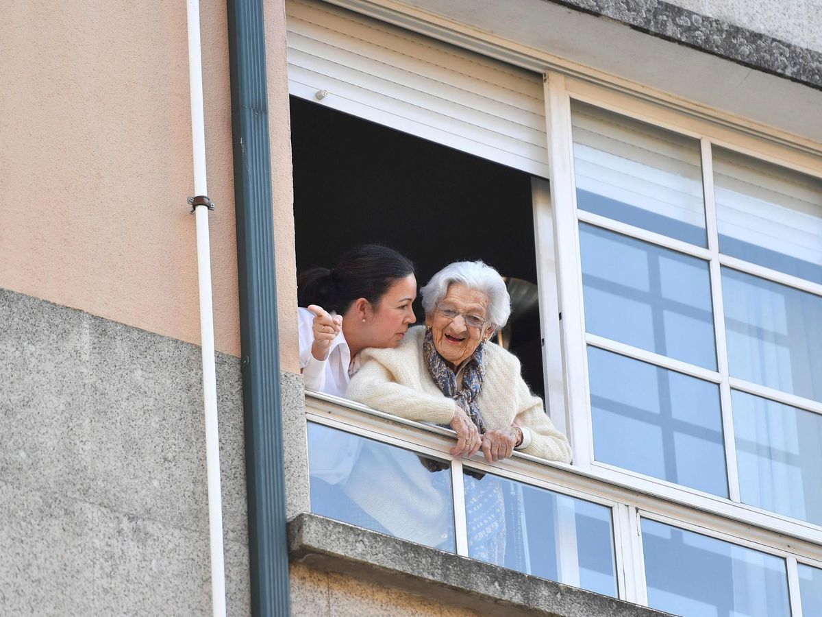 Foto: Lulú Vázquez (d), que cumplió ayer 110 años, saluda a sus vecinos que le están felicitando el cumpleaños confinada en su piso de Pontevedra (EFE)