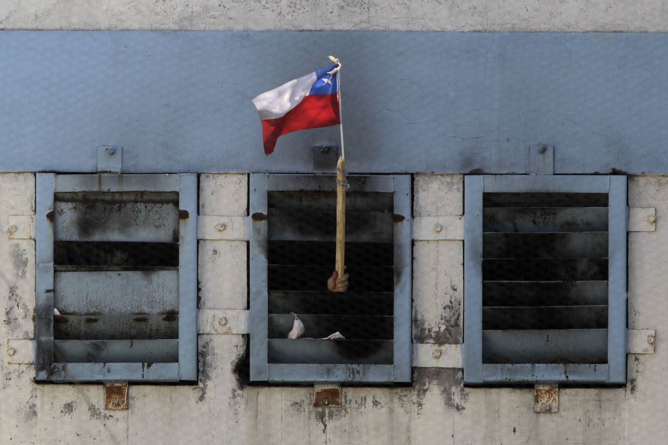 Un preso muestra una bandera chilena desde el interior de la prisión de San Miguel tras un incendio en el que murieron 81 reclusos, en Santiago de Chile. (Reuters)