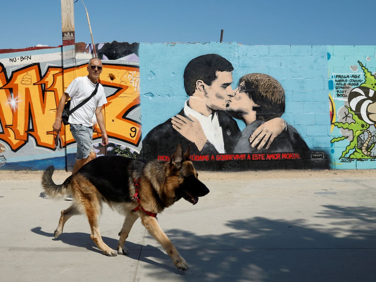 Foto: Hombre y perro pasan delante de un grafiti de Puigdemont y Sánchez besándose. (Reuters/Albert Gea)