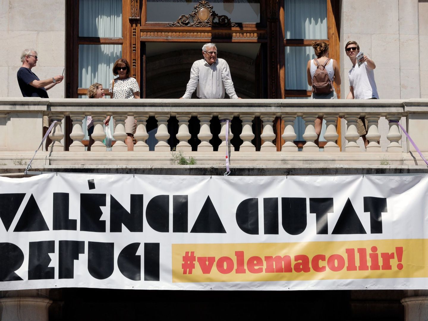 El alcalde de València, Joan Ribó, se asoma al balcón de la Plaza del Ayuntamiento tras la instalación de una gran pancarta con el lema 'Valencia, ciudad refugio'. (EFE)