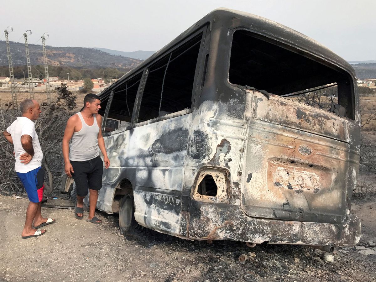 Foto: Varios hombres inspeccionan un autobús quemado tras un incendio forestal en El Kala, en la provincia argelina de Al Taref. Fotografía de archivo. (Reuters/Ramzi Boudina)