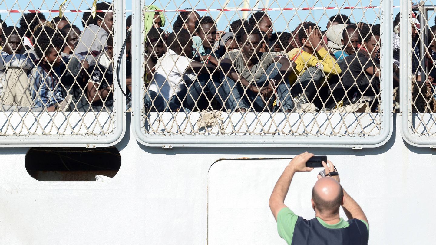 Un agente de policía fotografía a un grupo de inmigrantes que esperan para desembarcar en el puerto de Palermo. (Reuters)