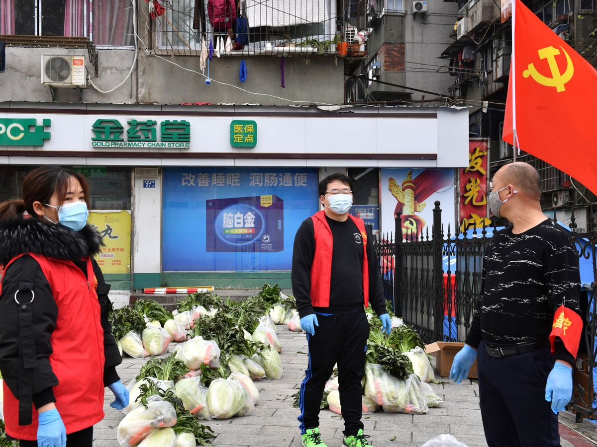 Foto: Voluntarios llevando mascarillas reparten verduras entre residentes de Wuhan (Reuters)