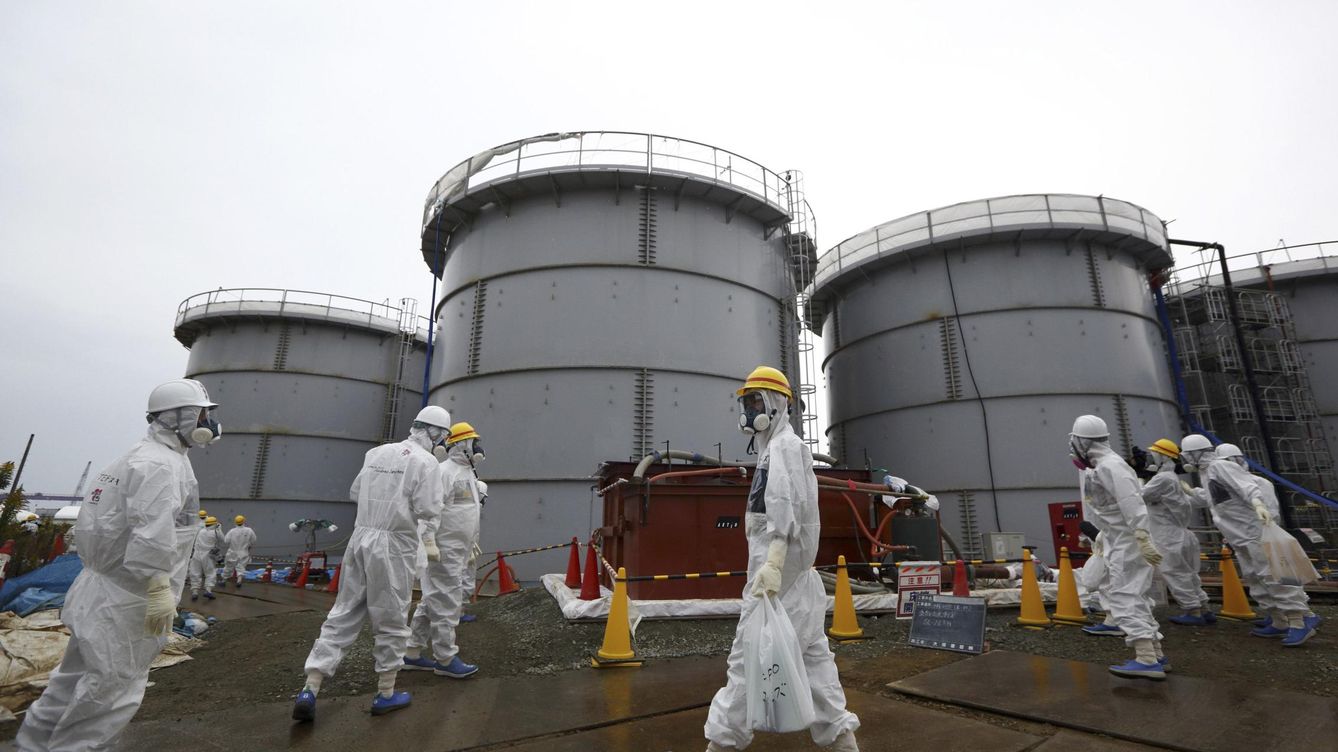 Foto: File photo of members of the media and tepco employees wearing protective suits and masks walking past storage tanks in fukushima prefecture