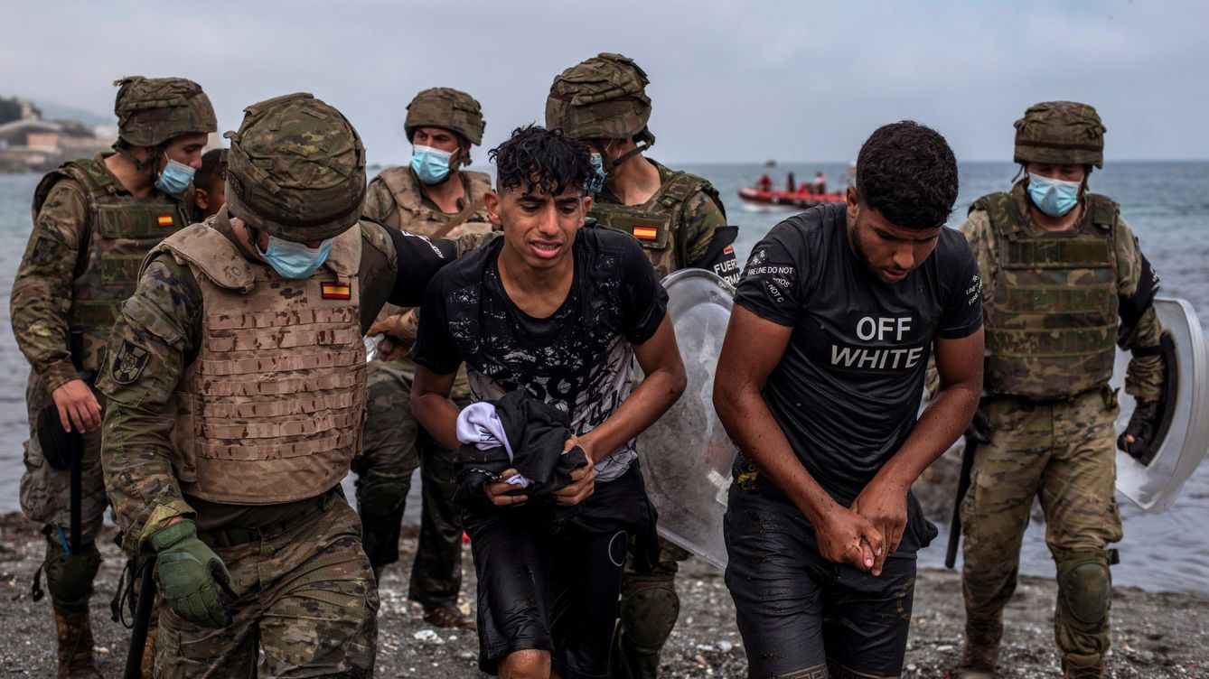 Foto: Soldados del Ejército con dos personas migrantes en la playa de El Tarajal, Ceuta. (EFE)