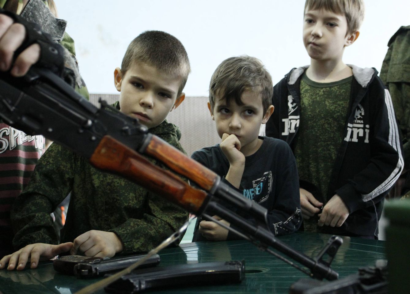Un combatiente de las milicias prorrusas de Donetsk muestra un rifle de asalto a unos niños durante unas jornadas educativas para menores, en Donetsk. (Reuters)