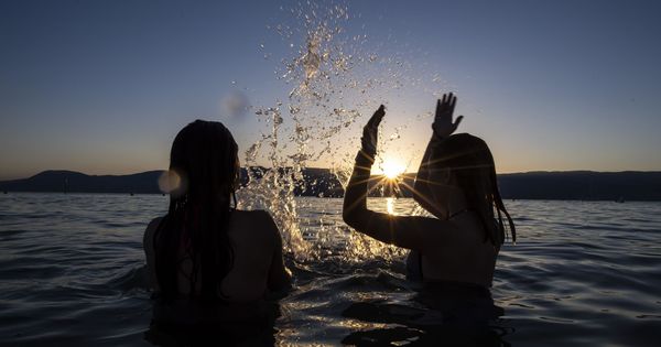 Foto: Dos adolescentes disfrutan de la puesta de sol en el agua (EFE)