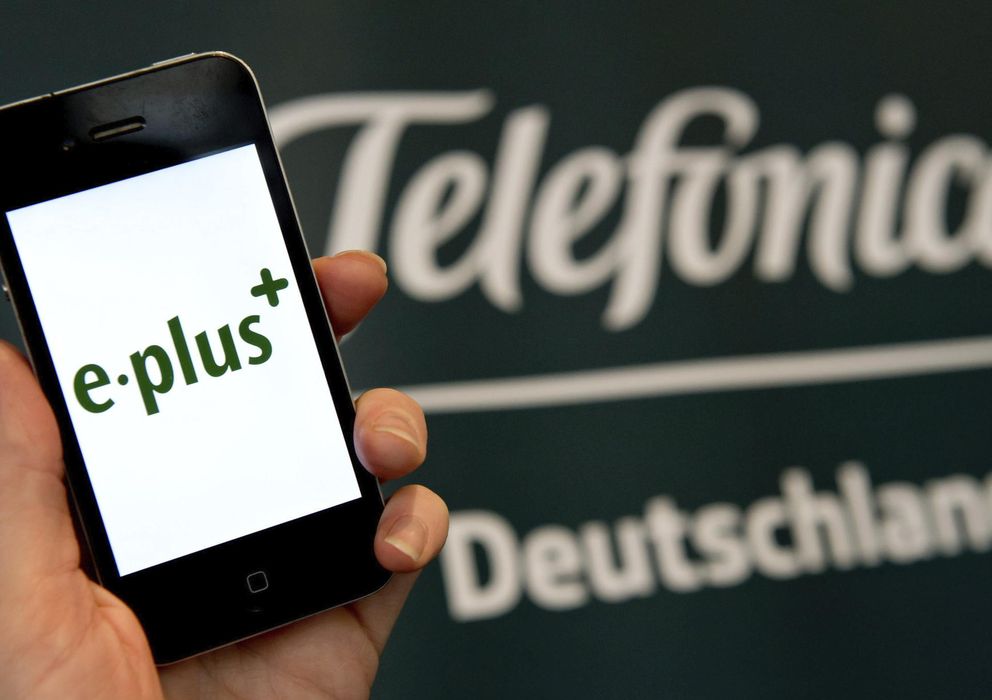 Foto: Una mujer sostiene un 'smartphone', en cuya pantalla aparece el logotipo de E-Plus frente a un cartel de Telefónica Deutschland. (EFE)