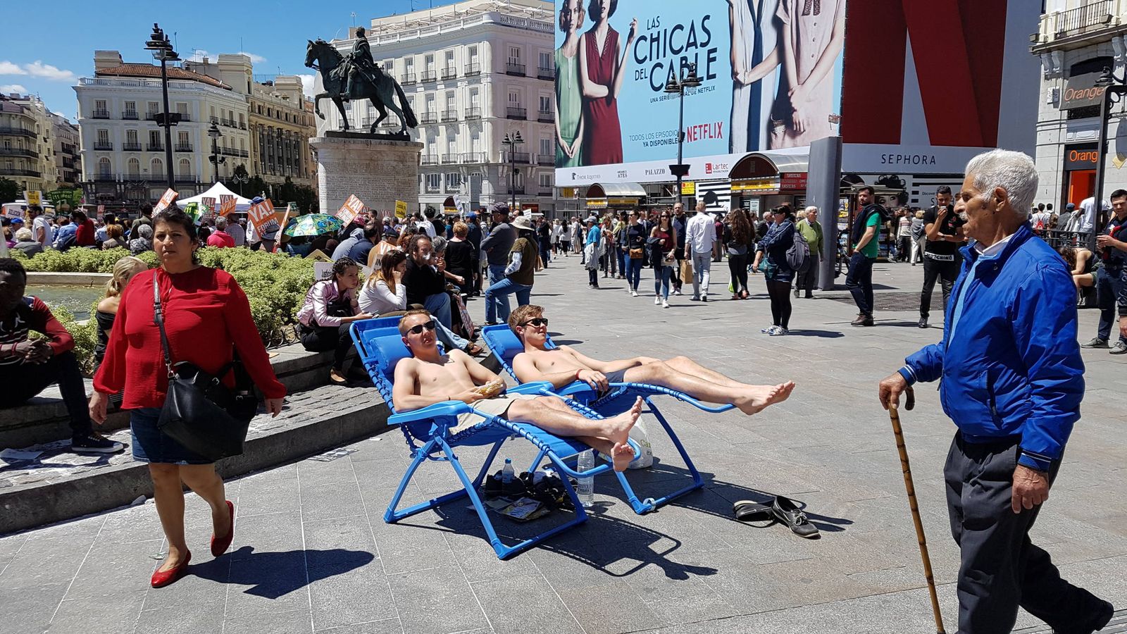 Foto: Dos turistas toman el sol semidesnudos en la Puerta del Sol de Madrid. (Henar Ortega)