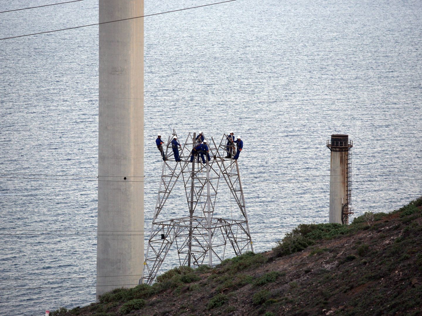 Varios técnicos reparan una torre de transporte de electricidad en alta tensión.