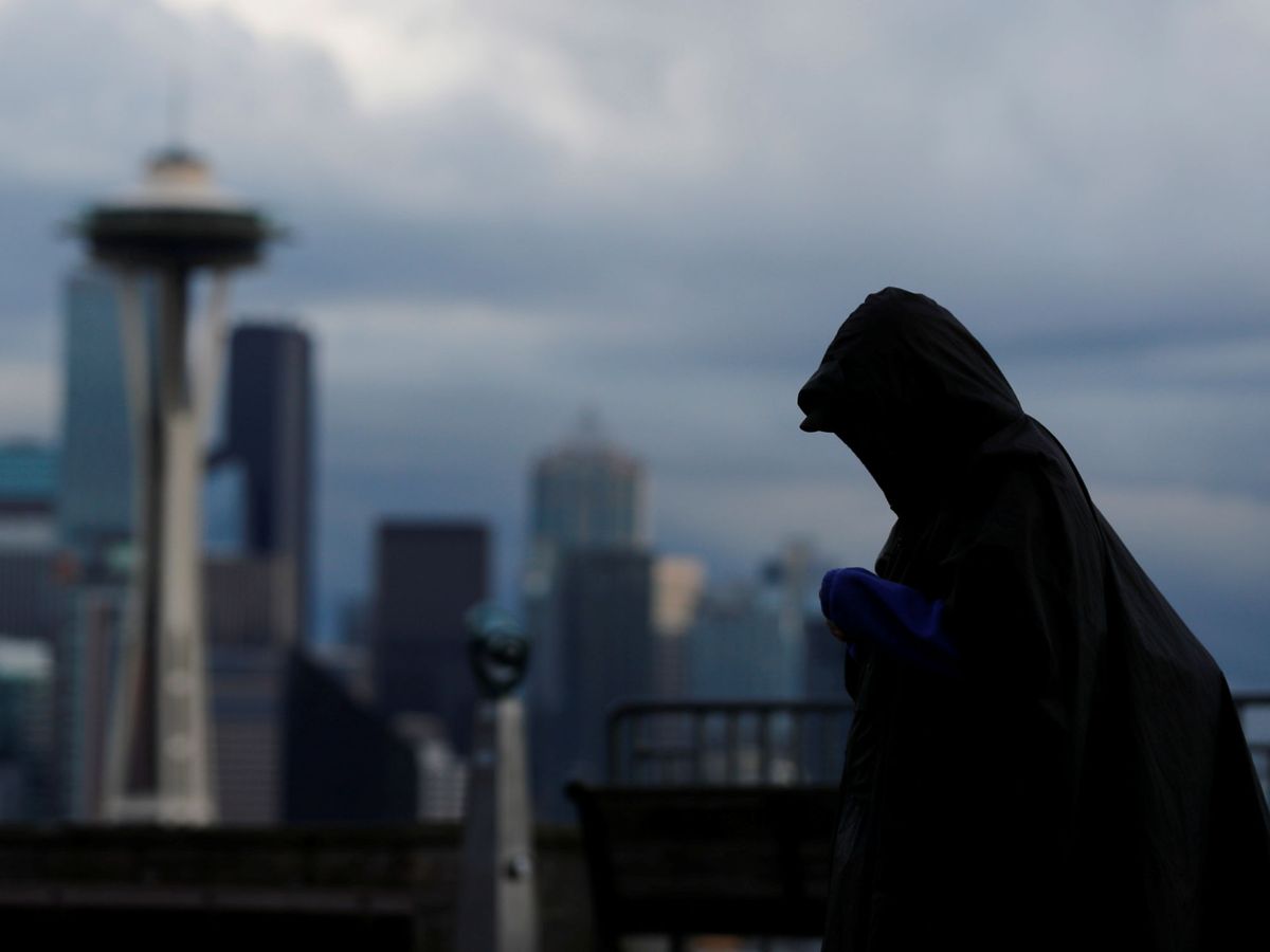 Foto: Un hombre con poncho camina frente al 'skyline' de Seattle. (Reuters/Brian Snyder)