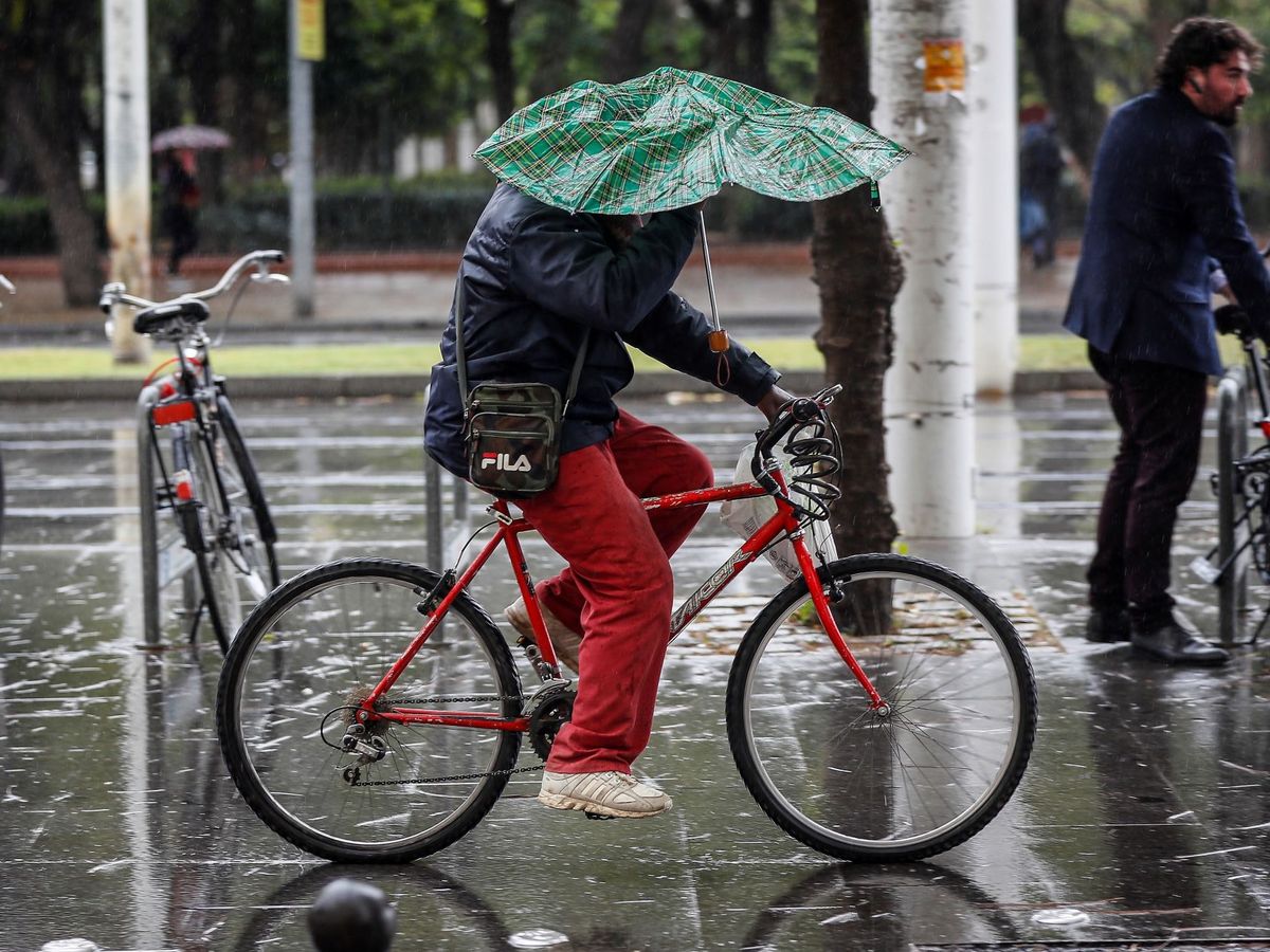 Foto: Una persona circula en bicicleta mientras intenta resguardarse de la lluvia. (EFE)