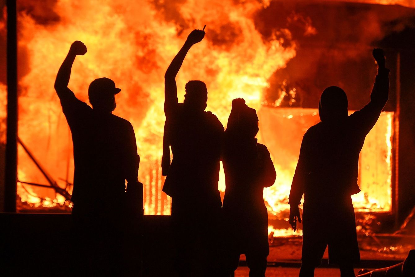 Manifestantes alzan el puño junto a una tienda en llamas, durante unos disturbios en Minneapolis. (EFE)