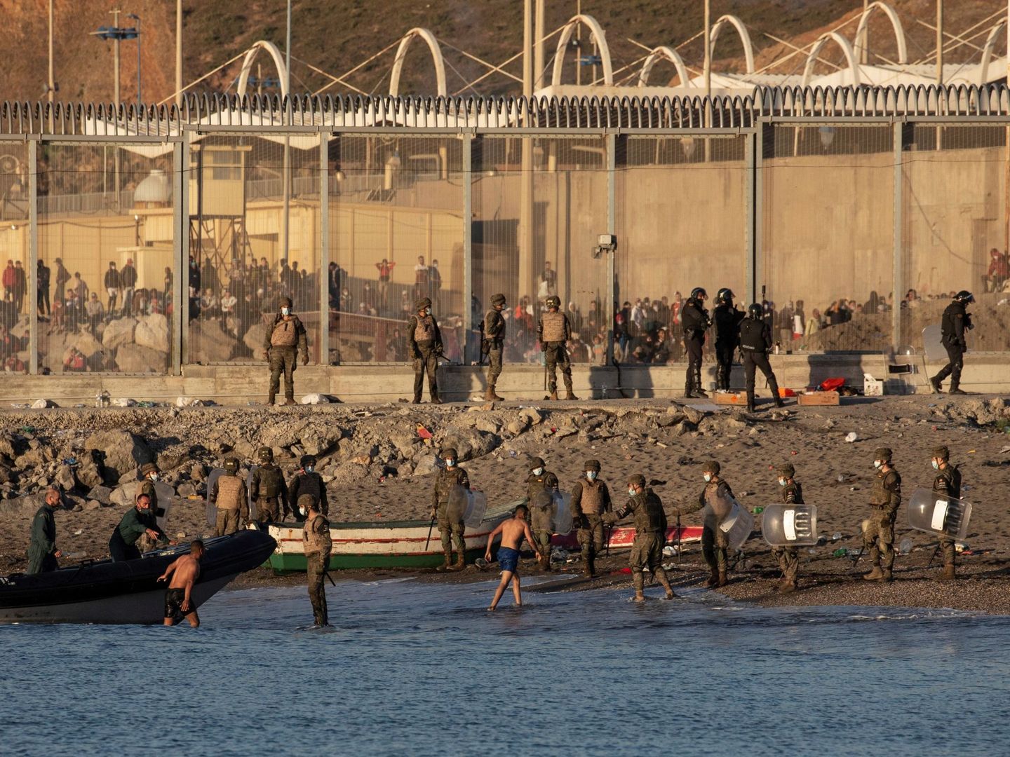 Miembros del Ejército ayudan a dos inmigrantes a su llegada a la playa de El Tarajal, junto a la valla fronteriza, en Ceuta. (EFE)