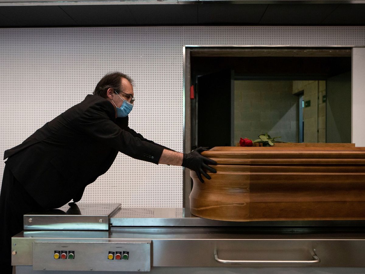Foto: Un trabajador de una empresa funeraria introduce un ataúd en un crematorio. (EFE/Enric Fontcuberta)