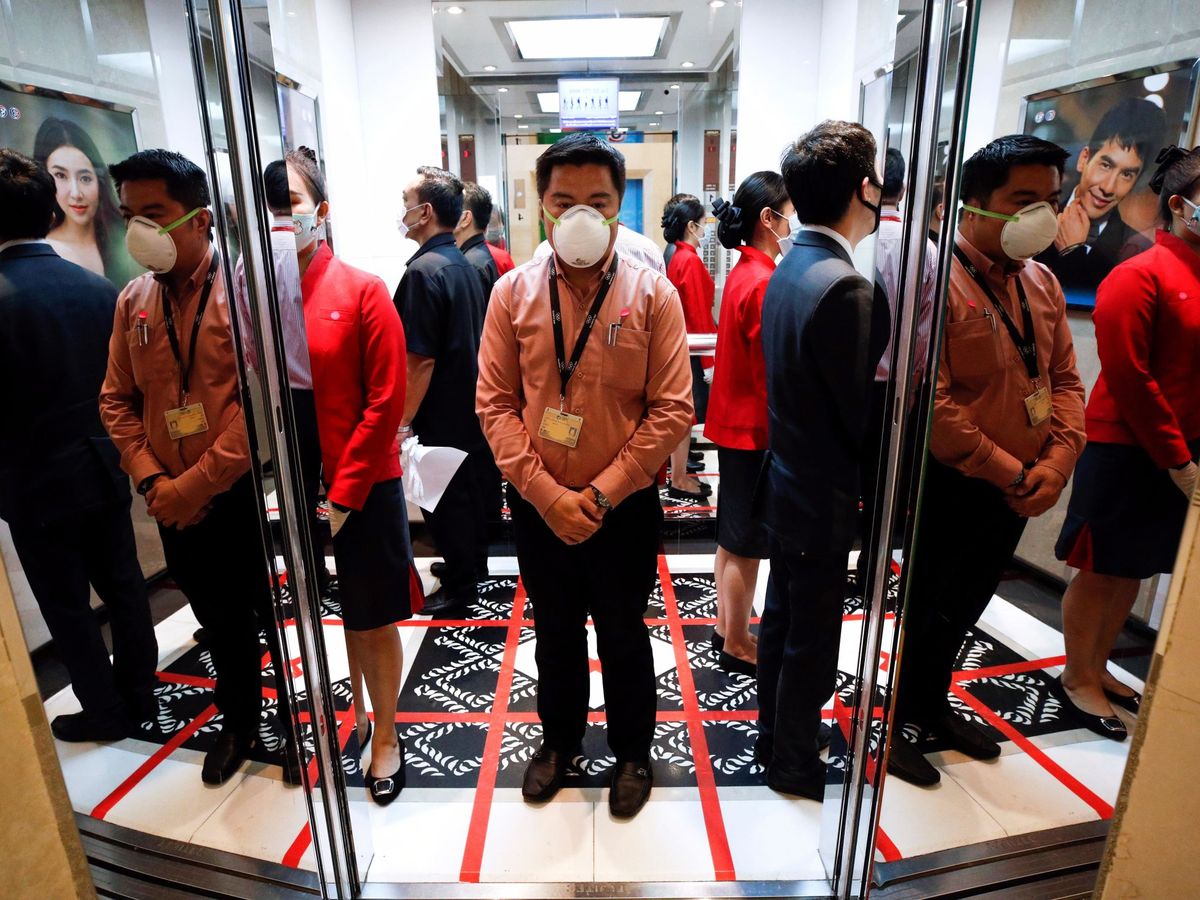 Foto: Empleados de oficina se protegen con mascarilla mientras esperan el ascensor sobre un cuadrante dibujado. (EFE / Rungroj Yongrit)