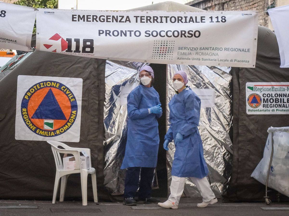 Foto: Dos sanitarios usan trajes protectores y máscaras de atención médica frente a la unidad médica avanzada construida fuera de la sala de emergencias del hospital Piacenza. (EFE)