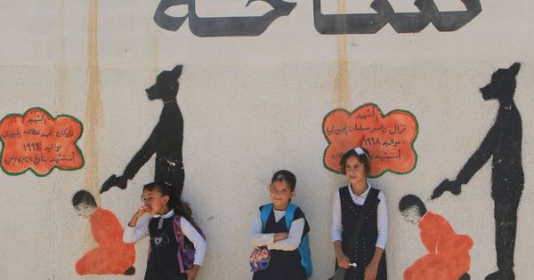 Foto: Niñas iraquíes frente a un muro escolar con dibujos de ejecuciones de prisioneros por el Estado Islámico, en Mosul, el 30 de abril de 2018. (Reuters)