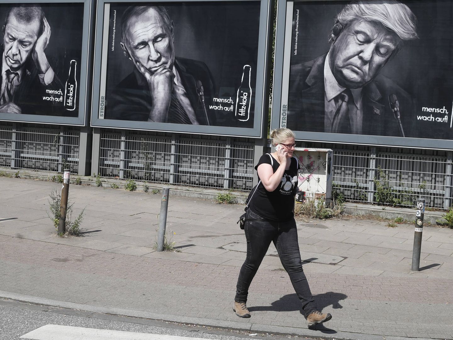 Una mujer pasa ante carteles que representan a Erdogan, Putin y Trump, en Hamburgo. (Reuters)