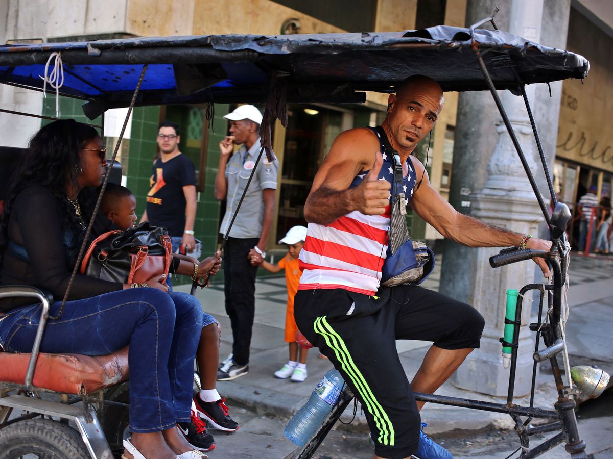 Foto: Un hombre vestido con una camiseta con la bandera de EEUU maneja un 'bicitaxi' en La Habana. (EFE)