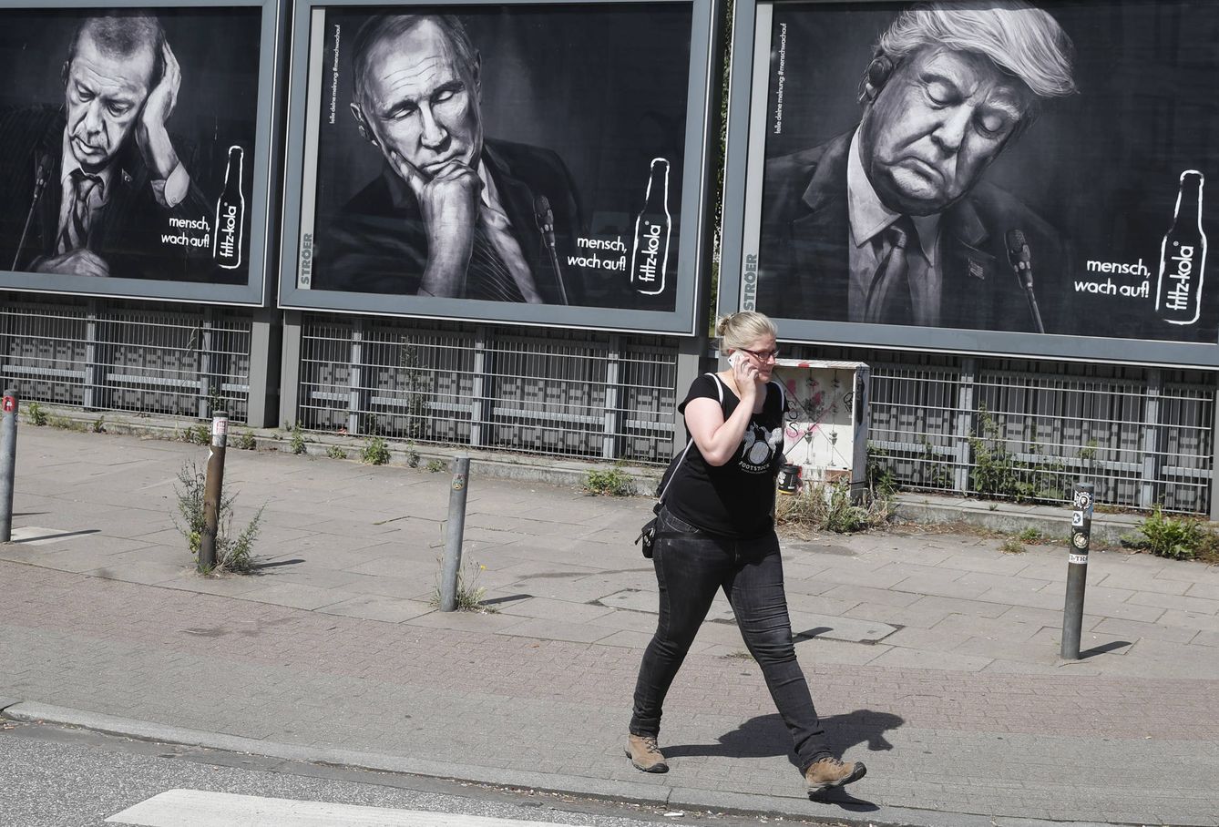 Una mujer pasa ante carteles que representan a Erdogan, Putin y Trump, en Hamburgo. (Reuters)