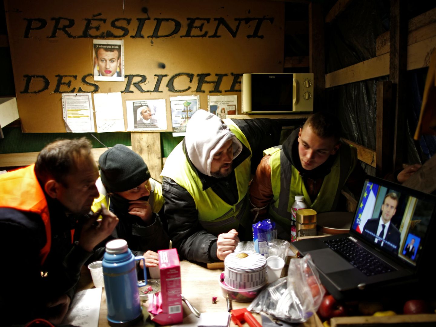 Un grupo de chalecos amarillos mira el discurso de Macron desde su campamento en Bouguenais. (Reuters)