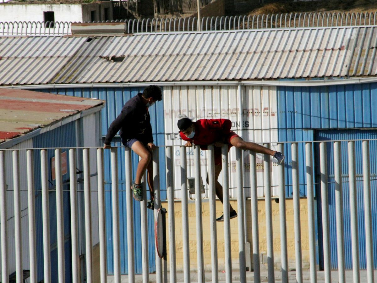 Foto: Dos menores marroquíes intentan saltar la valla del centro de Ceuta en el que estaban internados. (EFE)