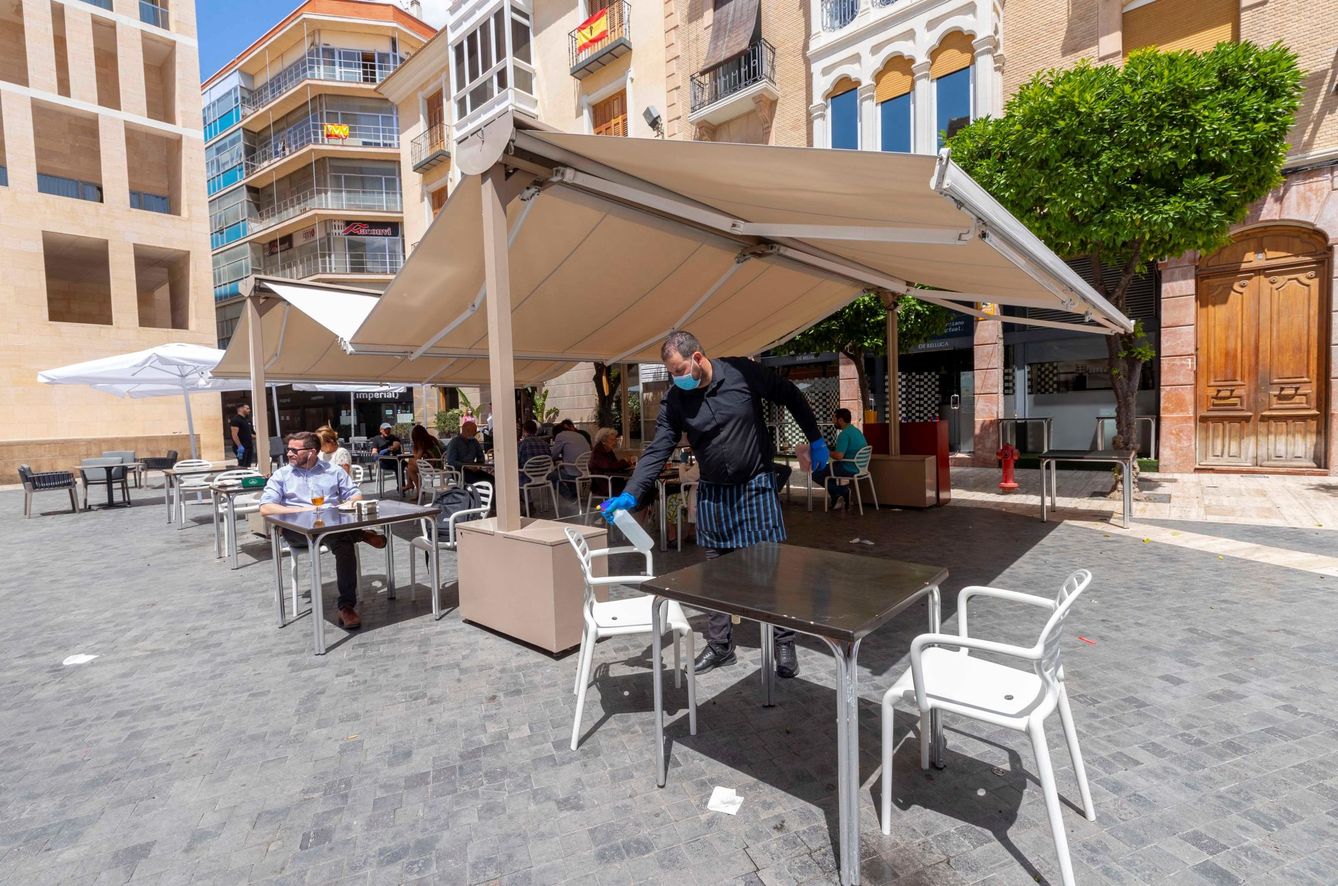 Un camarero desinfecta una mesa tras un servicio en una terraza de la Plaza del Cardenal Belluga de Murcia. (EFE)