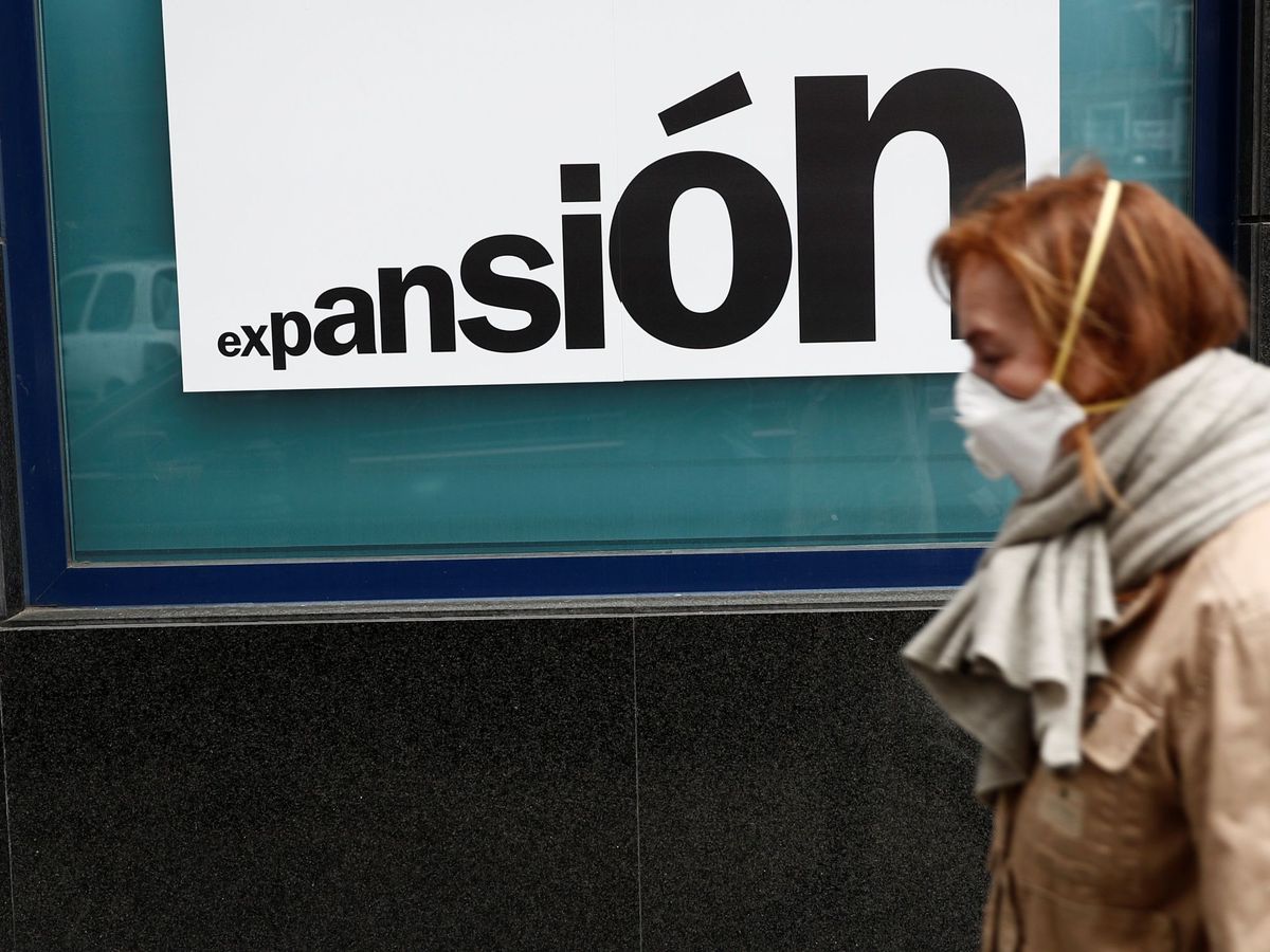 Foto: Una mujer con una mascarilla camina junto una sucursal bancaria de Madrid. (EFE)