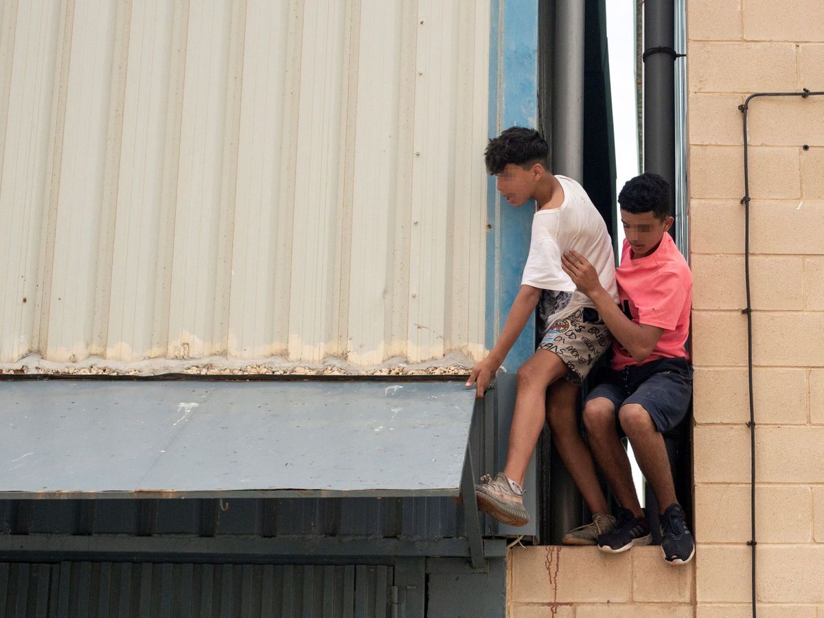 Foto: Dos migrantes se escapan de la nave del polígono industrial cercano a la playa de El Tarajal en mayo. (EFE)